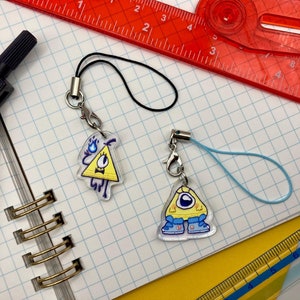 May include: Two clear acrylic charms with cartoon triangle designs. One charm has a yellow triangle with a bow tie and blue flames. The other has a yellow triangle with a single eye and blue shoes. Both have a silver clasp and a lanyard.