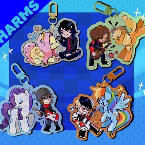 May include: Four acrylic charms featuring cartoon characters paired with ponies. One shows a person with a yellow pony, another a person playing guitar with an orange pony, a third a white pony with a person playing bass, and a fourth a blue pony with a person playing guitar.