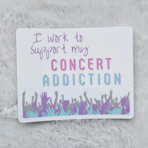 May include: White sticker with the text "I work to support my CONCERT ADDICTION" in purple and pink lettering. A crowd of people with raised hands is depicted in blue and purple.