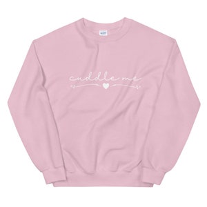 May include: A pink sweatshirt with the text "cuddle me" in white cursive lettering with a small heart symbol.