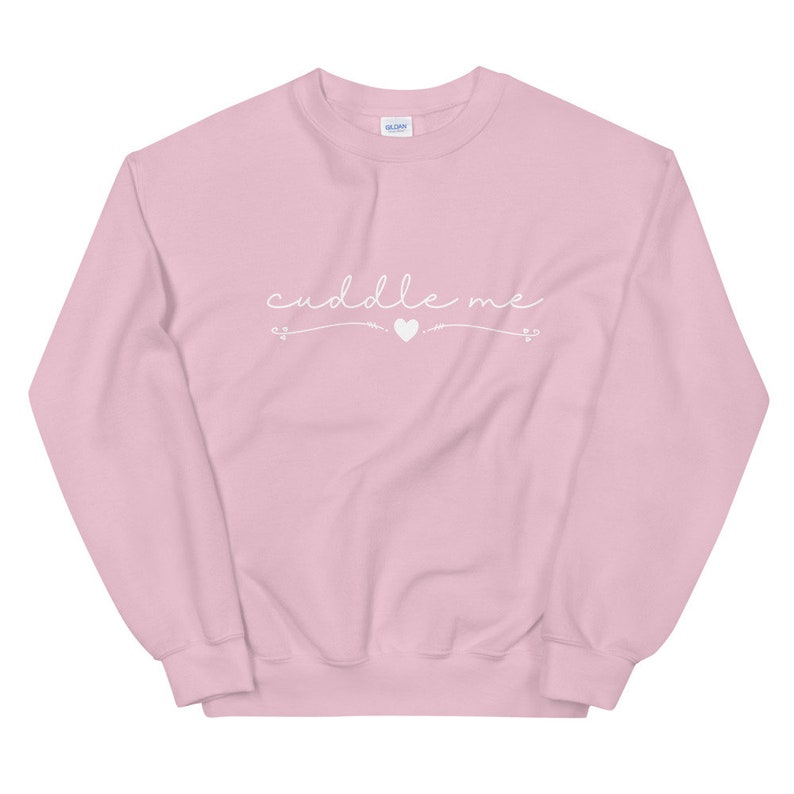 May include: A pink sweatshirt with the text "cuddle me" in white cursive lettering with a small heart symbol.