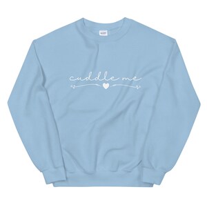 May include: Light blue sweatshirt with the text "cuddle me" in white cursive lettering with a small white heart in the middle.