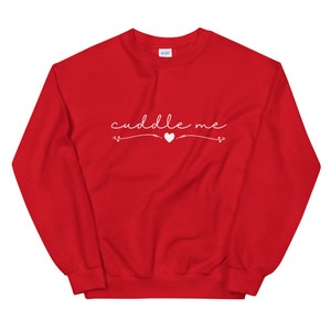 May include: Red sweatshirt with the text "cuddle me" in white cursive lettering with a small white heart in the middle.