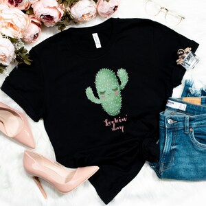 May include: Black t-shirt with a green cactus graphic and the text "Lookin' sharp" in pink.