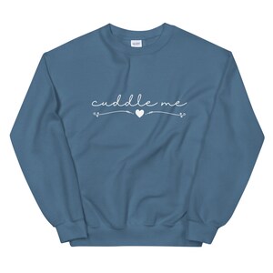 May include: A blue sweatshirt with the text "cuddle me" in white cursive lettering with a small heart and arrows on either side.