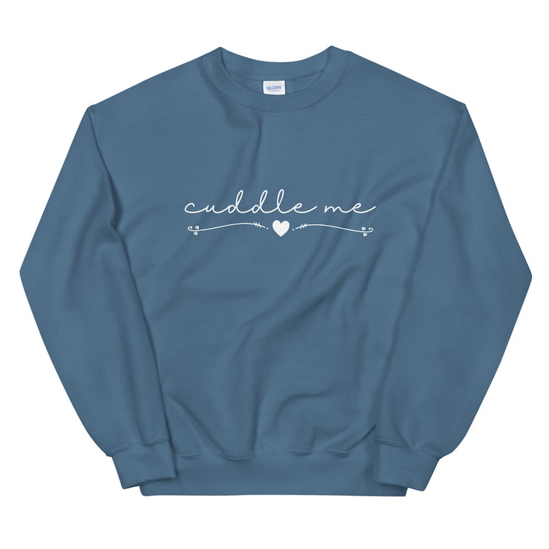 May include: A blue sweatshirt with the text "cuddle me" in white cursive lettering with a small heart and arrows on either side.