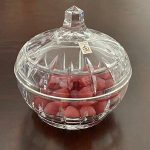 May include: A clear glass candy dish with a lid, filled with pink heart-shaped candies. The dish has a cut-glass design and a sticker on the lid that reads "Polka Crystal".