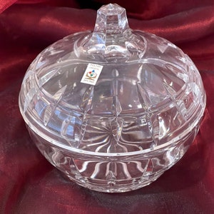 May include: A clear glass candy dish with a lid. The dish has a cut glass design and is decorated with a label that reads "Poltar Crystal 24% PbO".