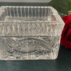 Op de afbeelding: Een vierkante doos van helder glas met ingewikkelde geslepen glasontwerpen. De doos heeft een verhoogde rand en een decoratief patroon op de bodem.