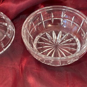 May include: A clear glass bowl with a cut crystal design. The bowl has a starburst pattern in the center and a geometric pattern around the rim.