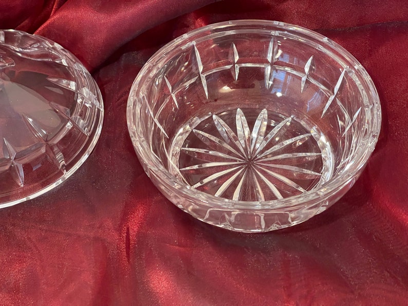 May include: A clear glass bowl with a cut crystal design. The bowl has a starburst pattern in the center and a geometric pattern around the rim.
