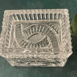 Op de afbeelding: Een rechthoekige glazen doos met een decoratief, geslepen glasontwerp. De doos heeft een vierkante basis en een licht verhoogde rand.