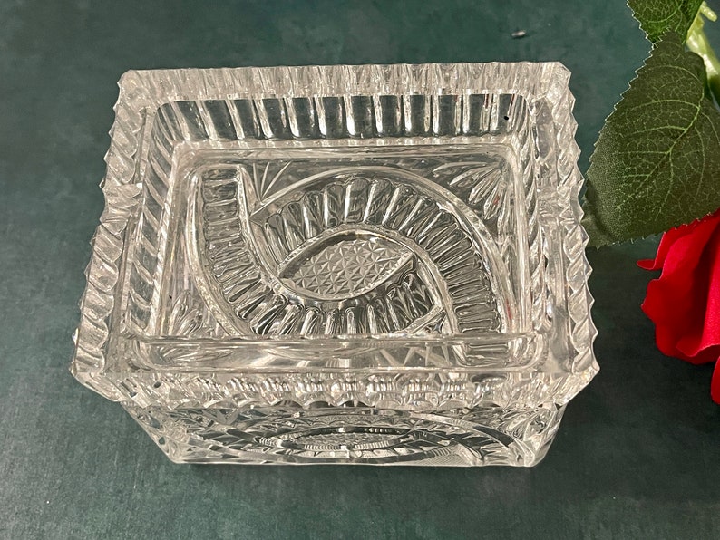 Op de afbeelding: Een rechthoekige glazen doos met een decoratief, geslepen glasontwerp. De doos heeft een vierkante basis en een licht verhoogde rand.