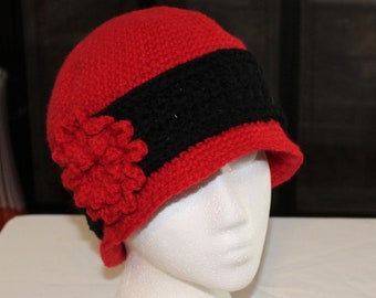 May include: A red and black crocheted hat with a flower detail. The hat has a wide brim and is made with a textured stitch.