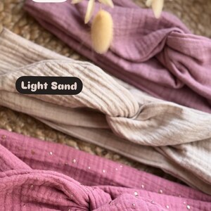 Könnte beinhalten: Drei Stoff-Haarband in verschiedenen Farben und Mustern. Das obere Haarband ist einfarbig rosa, das mittlere Haarband ist hellbeige und das untere Haarband ist rosa mit goldenen Glitzerpunkten. Die Haarband sind mit "Rosa", "Light Sand" und "Rosa & Gold" beschriftet.