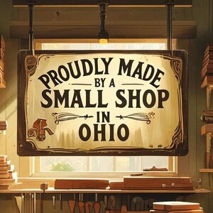 May include: A sign reading "Proudly Made by a Small Shop in Ohio" hangs in a workshop. The sign is brown with black lettering. Shelves hold stacks of wood and tools.