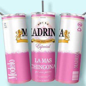 May include: A pink and white stainless steel tumbler with a design that resembles a beer can. The design features the text "Soy La Madrina" and "La Mas Chingona" with a lion logo. The tumbler is 20 fluid ounces.