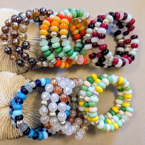 May include: A collection of multi-strand wrap bracelets featuring various bead styles, including faceted dark brown, clear, and amber glass beads, alongside smooth opaque beads in vibrant orange, yellow, green, blue, pink, white, black, and red.
