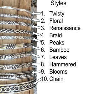 May include: Ten different styles of silver bangle bracelets, each with a unique textured design. The styles are labeled: Twisty, Floral, Renaissance, Braid, Peaks, Bamboo, Leaves, Hammered, Blooms, and Chain.
