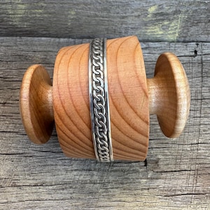 May include: A wooden spool with a silver chain wrapped around it. The spool is made of light wood and has a smooth finish.