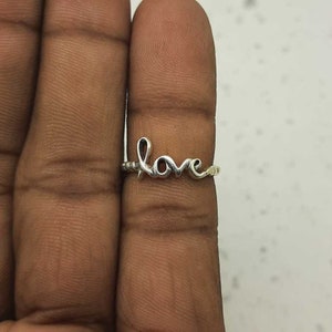 May include: A silver ring with the word "love" written in a cursive font.