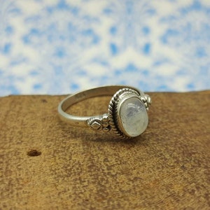 May include: A silver ring with a white moonstone oval cabochon set in a silver bezel. The ring has a decorative band with small silver beads and a rope-like design.