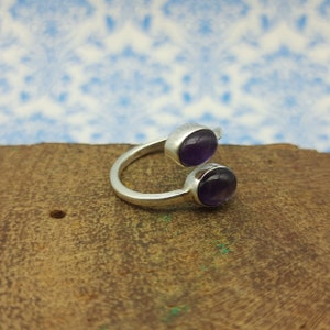 May include: A silver ring with two round amethyst stones. The ring is open and has a simple design.