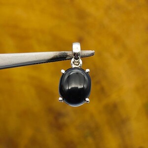 May include: A silver pendant with a black oval gemstone. The pendant is set in a silver bezel with four prongs.