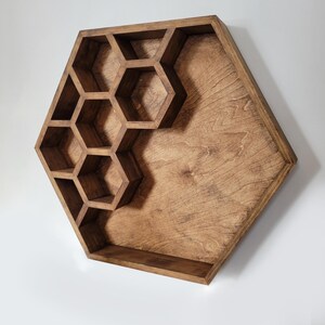 May include: A hexagonal wooden shelf with honeycomb-shaped compartments. The shelf is made of dark brown wood and has a rustic finish.
