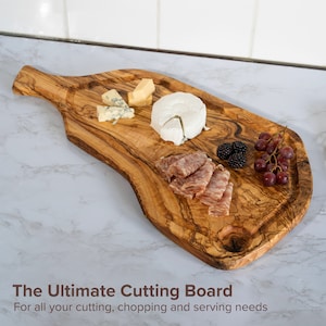Puede incluir: Tabla de cortar de madera con asa, con queso, embutidos, moras y uvas. El texto en la parte inferior dice "The Ultimate Cutting Board".