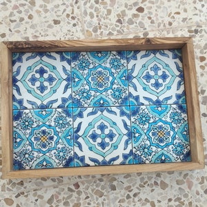 May include: Wooden serving tray with six square ceramic tiles. The tiles feature a blue and white floral pattern. The tray's frame is made of light-coloured wood. The tiles have a repeating design with a central flower.