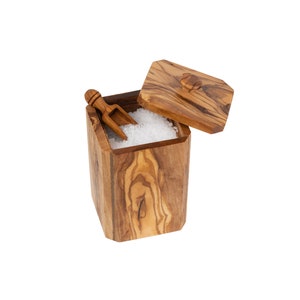 May include: A wooden salt cellar with a lid and a small wooden scoop. The cellar is filled with white salt.