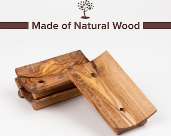 Puede incluir: Cuatro jaboneras de madera natural, hechas de madera de olivo, con forma curva y un agujero en el centro. Las jaboneras están apiladas una encima de la otra, con una jabonera tendida sobre la mesa. El texto "Made of Natural Wood" está impreso en una barra marrón sobre las jaboneras.