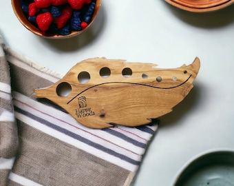 May include: Wooden leaf-shaped knitting needle holder with six holes and the text "Happy Woods" engraved on the surface.