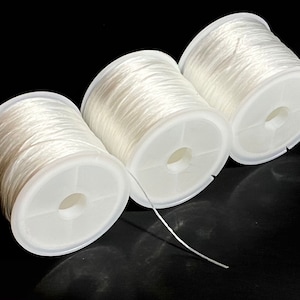 May include: Three spools of white thread wound around plastic bobbins. The thread is thin and appears to be nylon.
