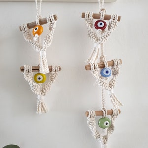 May include: Three macrame wall hangings with wooden dowels and evil eye beads. The top bead is red, the middle bead is blue, and the bottom bead is green.