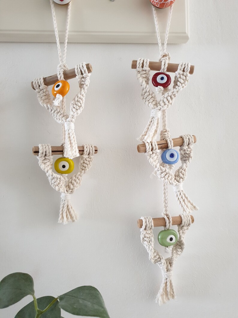 May include: Three macrame wall hangings with wooden dowels and evil eye beads. The top bead is red, the middle bead is blue, and the bottom bead is green.