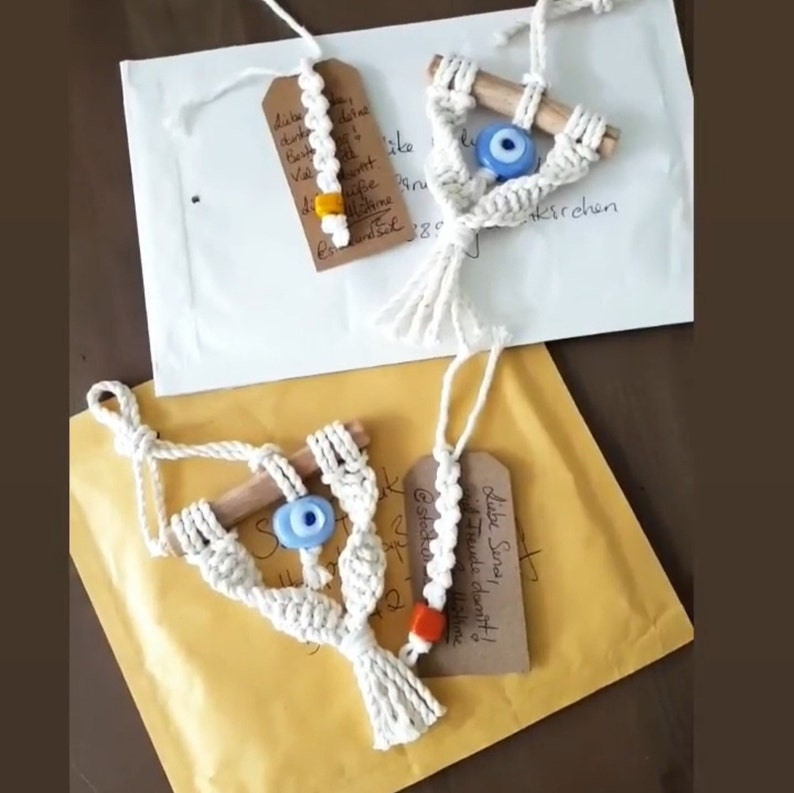 May include: Three white macrame wall hangings with blue evil eye beads and wooden dowels. The hangings are packaged and ready to ship. The tag reads "Liebe, Sonnenschein & Freunde!"