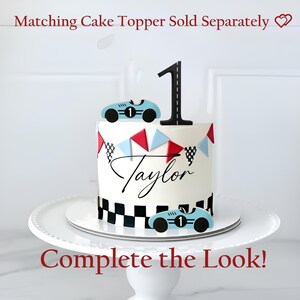 May include: A white cake with a black number one cake topper and two light blue race car toppers. The cake is decorated with red, blue, and black and white checkered flags and the name "Taylor". The cake sits on a white cake stand.