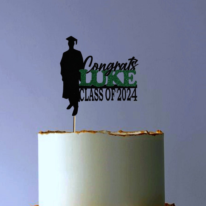 May include: Black and green graduation cake topper with a silhouette of a graduate, the text "Congrats Luke Class of 2024", and a small wooden stick.