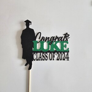 May include: Black silhouette of a graduate with a cap and gown, a green glitter 'LUKE' and the text 'Congrats Class of 2024'.