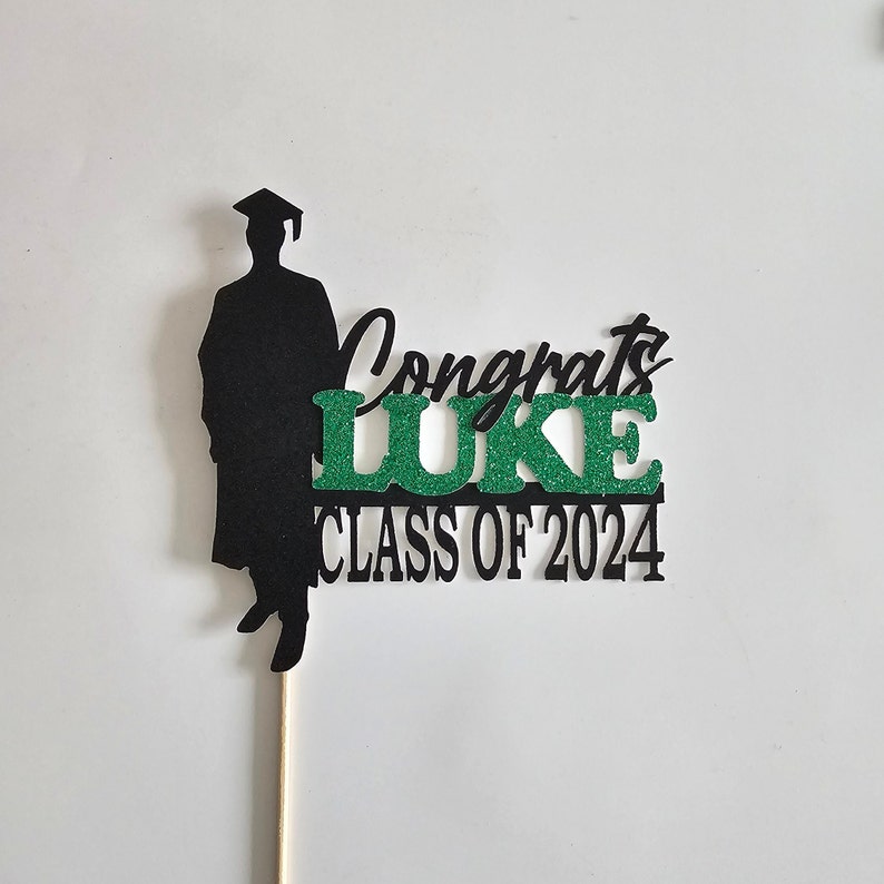 May include: Black silhouette of a graduate with a cap and gown, a green glitter 'LUKE' and the text 'Congrats Class of 2024'.