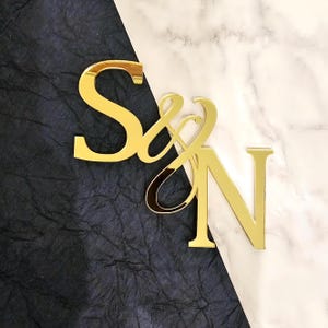 May include: Gold mirror acrylic letters spelling "S&N" on a black and white background.