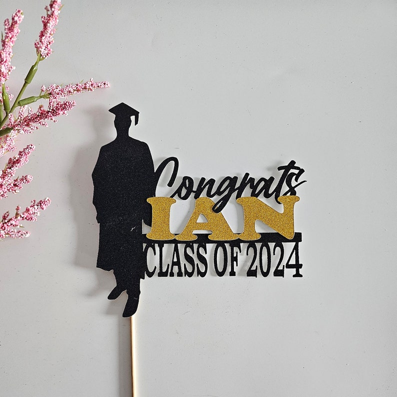 May include: Black silhouette of a graduate with a cap and gown, with gold glitter text that reads "Congrats Ian Class of 2024".