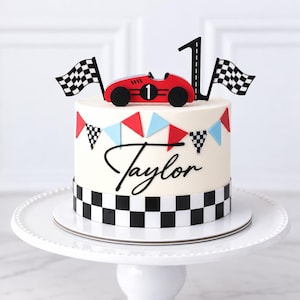 May include: A white cake decorated with a black and white checkered border, a red race car topper with the number one, a black number one, two checkered flags, and a string of red and blue pennants. The name Taylor is written in black script.