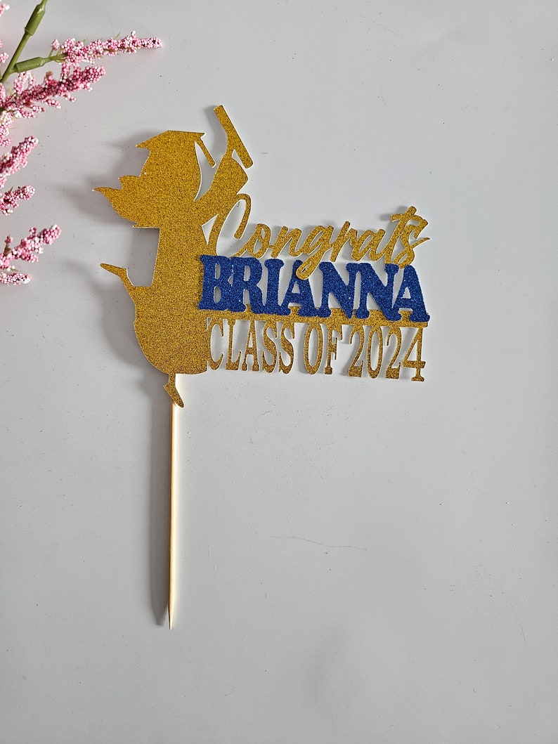 May include: Gold glitter graduation cap cake topper with the text "Congrats Brianna Class of 2024".