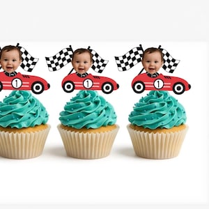 May include: Three cupcakes with teal frosting and racing car toppers. Each cupcake has a red race car with a baby's face and a checkered flag. The race cars have the number 1 on them.