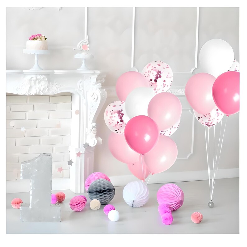 Puede incluir: Una escena festiva con globos rosas y blancos, globos llenos de confeti y bolas decorativas de papel. Un pastel blanco con flores rosas est&aacute; sobre un pedestal. Un gran n&uacute;mero uno plateado y pompones rosas completan la decoraci&oacute;n.