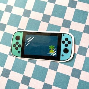 May include: A teal blue Nintendo Switch console sticker with a pixelated island and palm tree on the screen. The sticker is on a checkered background.