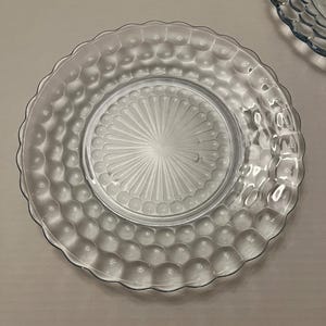 Puede incluir: Platos de vidrio transparente con un patrón de burbujas texturizadas alrededor del borde y un diseño de rayos de sol en el centro. Los platos tienen un borde festoneado y son adecuados para servir alimentos.